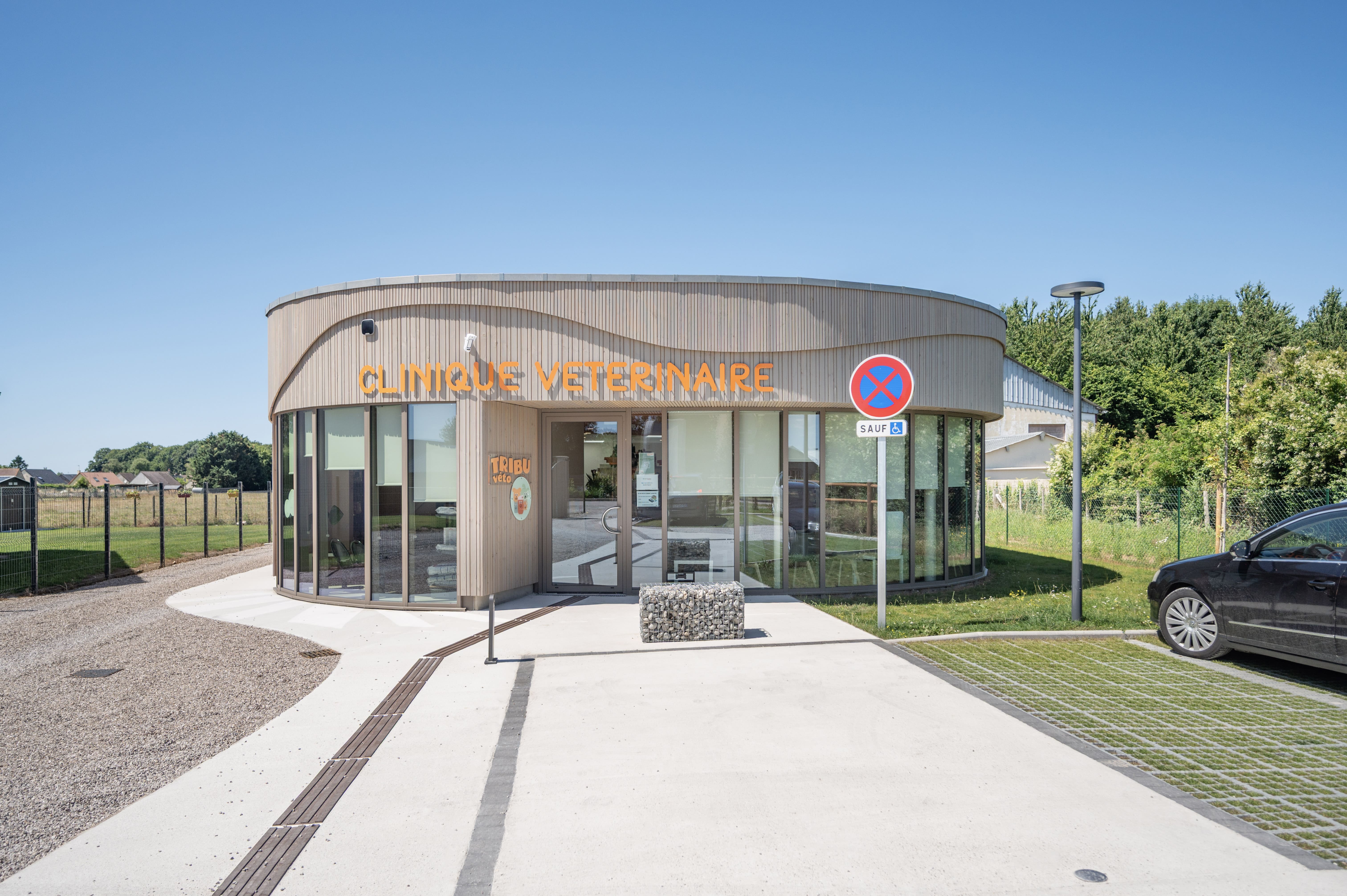 Vue d'ensemble de la Clinique Vétérinaire Tribu Véto avec sa façade en bois clair et son jardin environnant sous un ciel bleu.